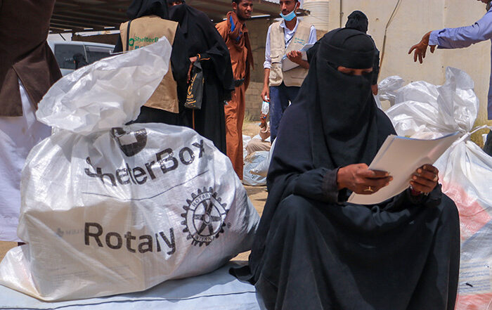 Woman reading a piece of paper sat next to a bag of aid from ShelterBox and Rotary