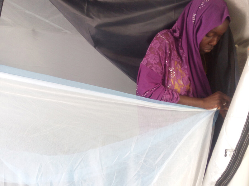 Woman zipping a mosquito net into a tent in Cameroon