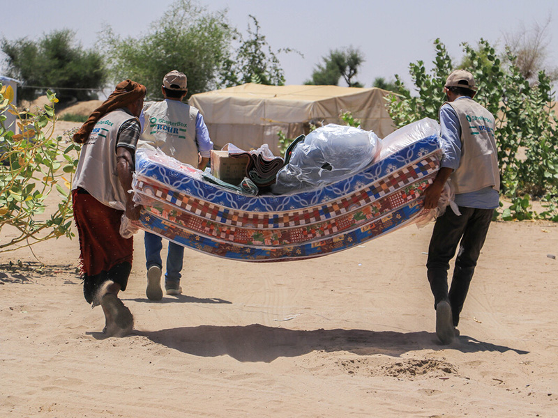 Three people carrying mattresses and other aid in Yemen