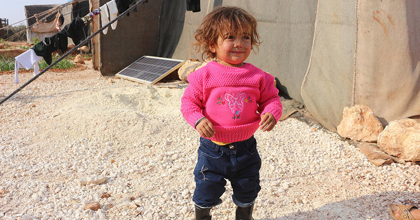 Small child in warm winter clothes next to tents in Syria