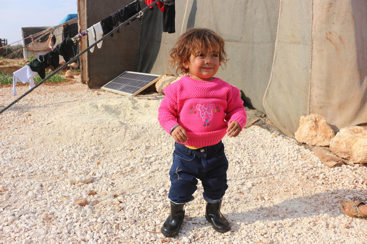 Child in warm jumper and trousers in a displacement camp in Syria