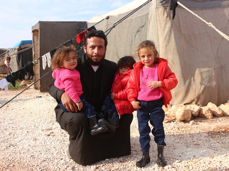 Man with three children wearing warm winter clothes in a Syrian displacement camp