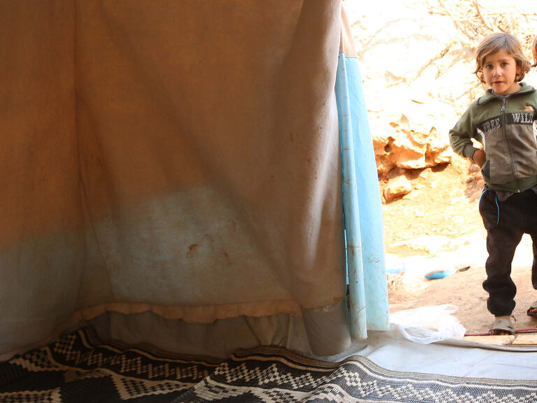 Two children standing in the doorway of a tent in Syria