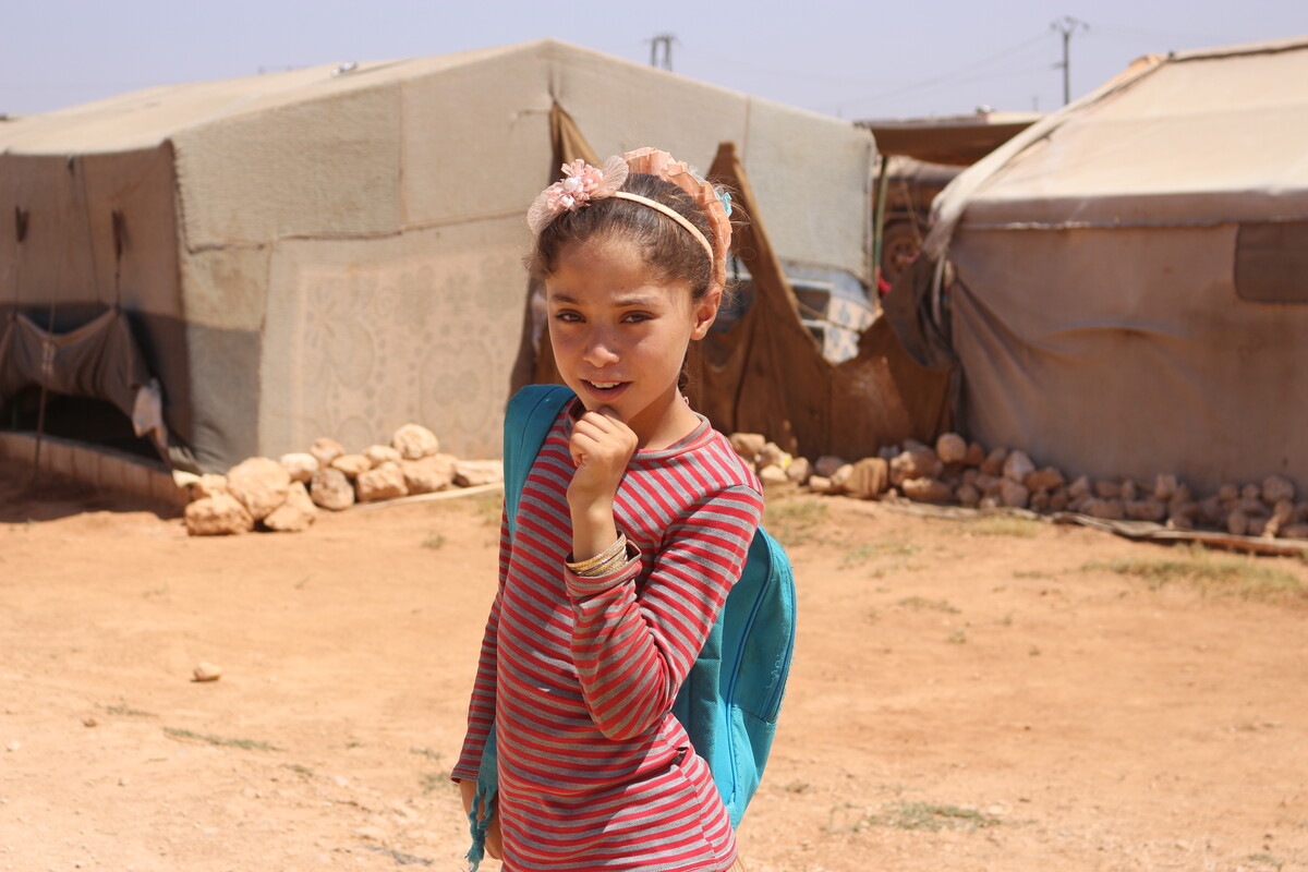 Girl carrying school bag in front of tents in Syria