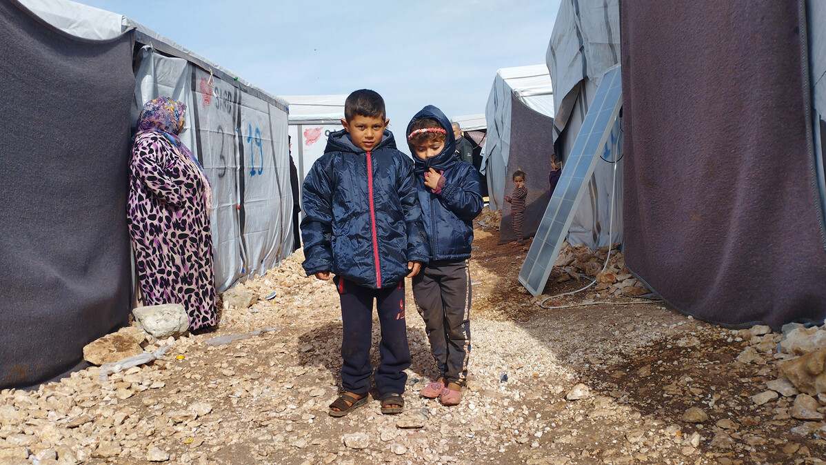 Two young boys wearing warm winter coats among tents in Syria