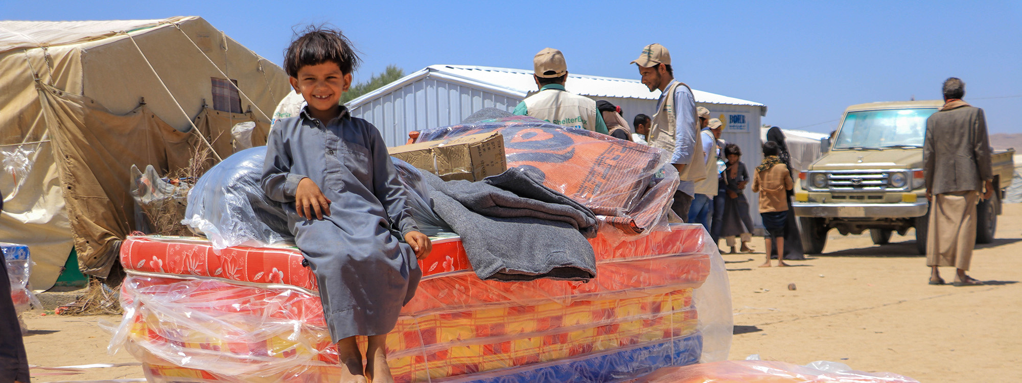 Boy sitting on top of mattresses and other ShelterBox aid in Yemen