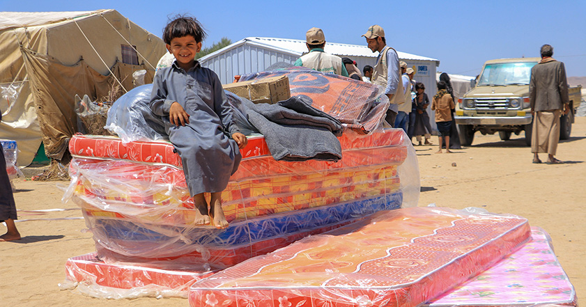 Boy sitting on top of mattresses and other aid in Yemen