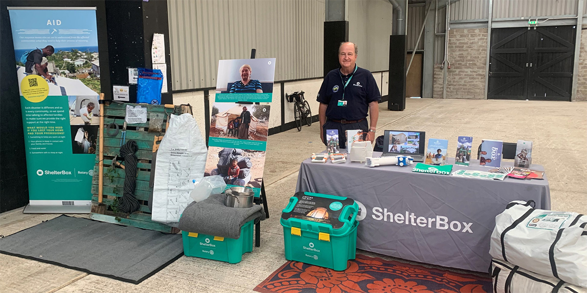 ShelterBox volunteer standing at a table with display items