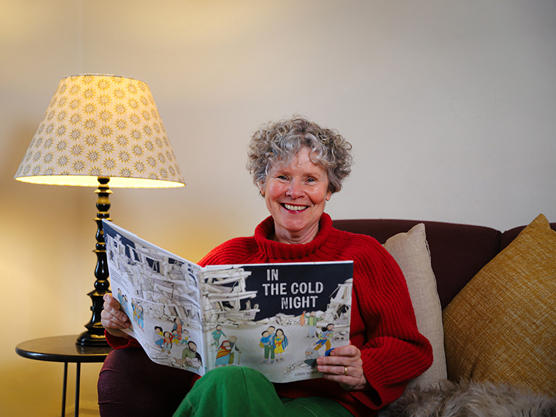 Image of Imelda Staunton sitting on a sofa holding a book titled 'In the Cold Night'