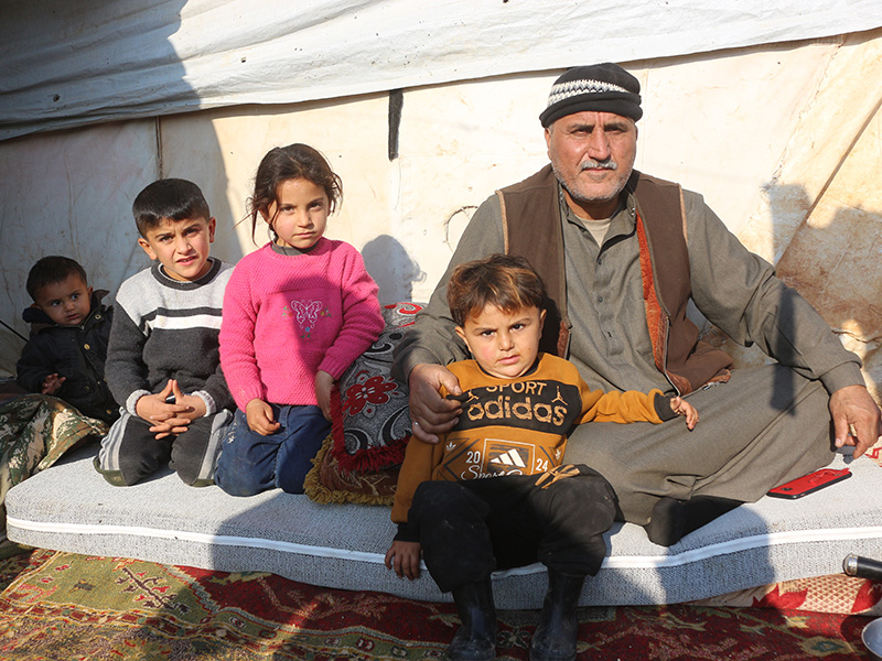 Man with 4 children sitting outside a tent in Syria
