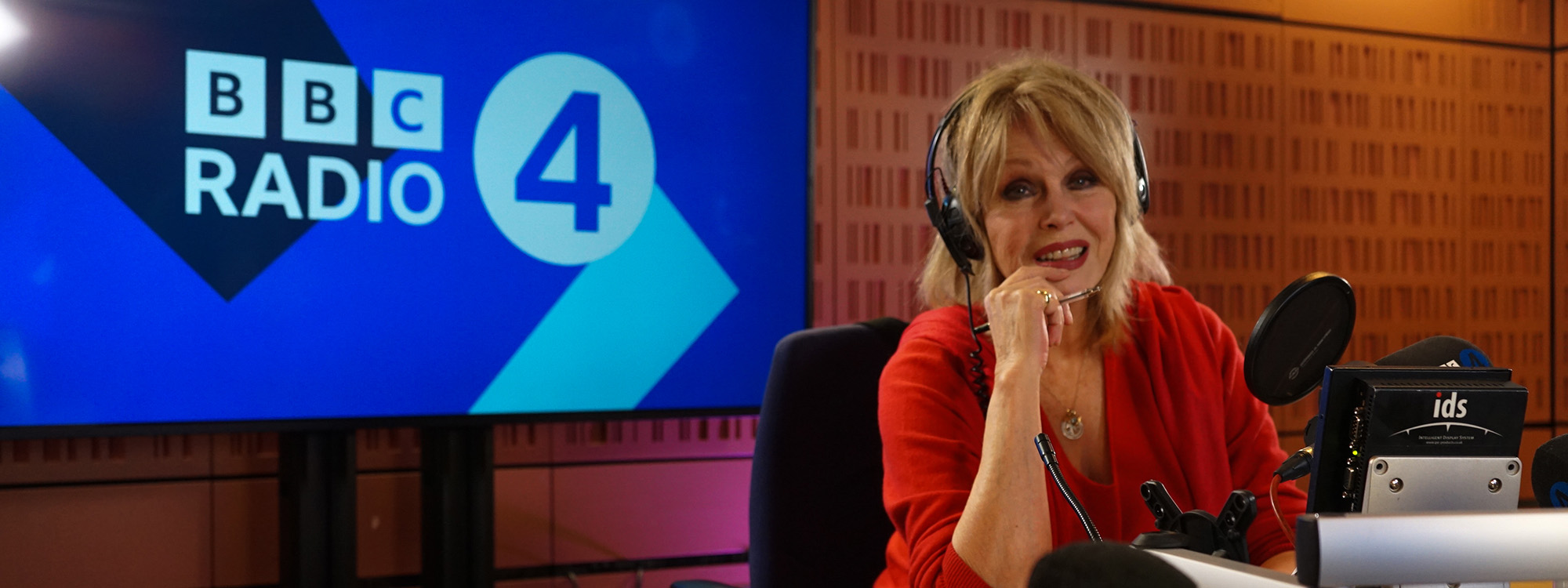 Joanna Lumley sitting in a recording booth with 'BBC Radio 4' on a screen behind her