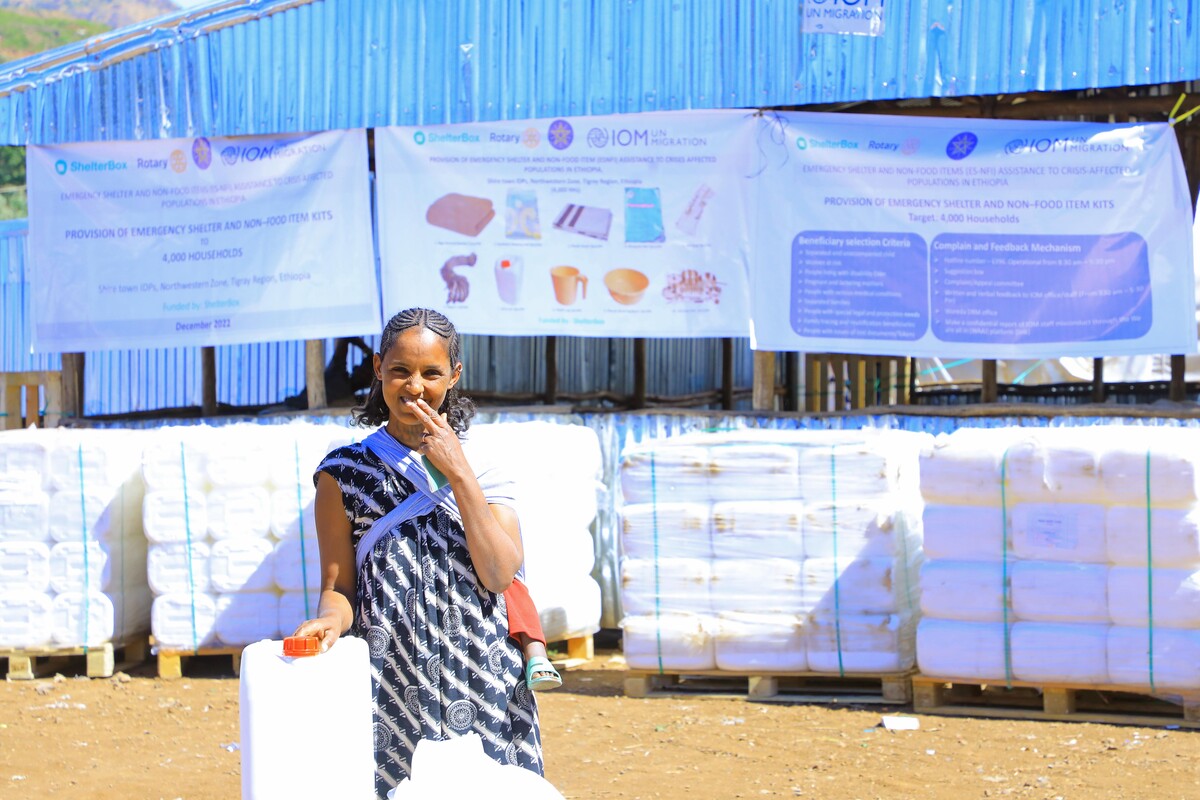 Woman holding a water carrier in front of aid packages in Ehtiopia