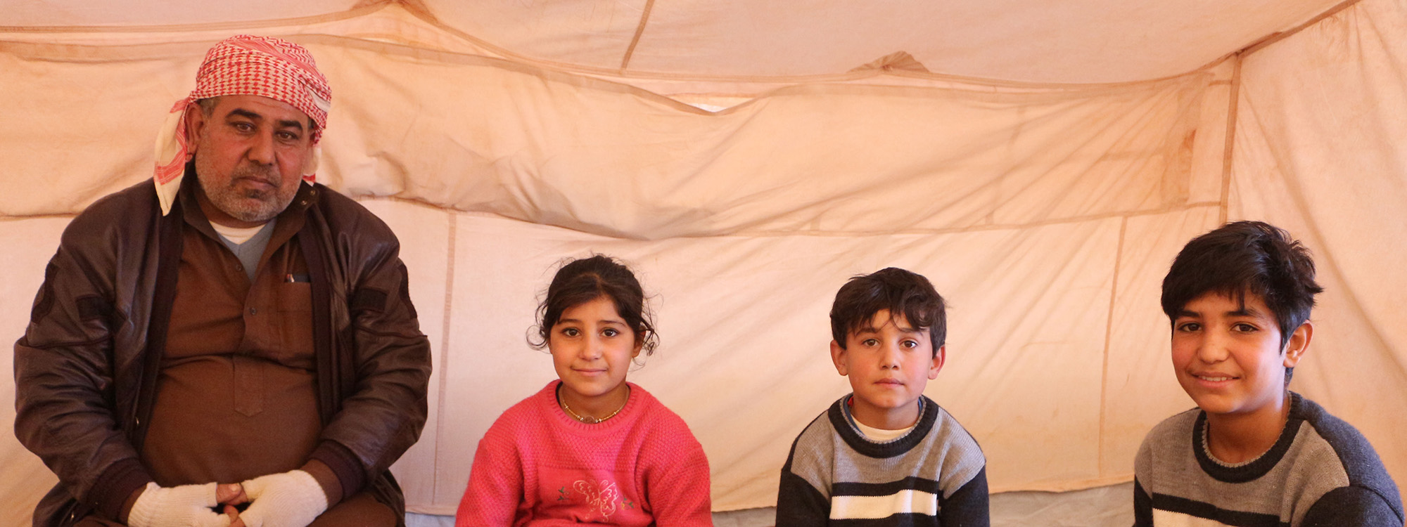 Man and three children wearing winter clothes in a tent in Syria