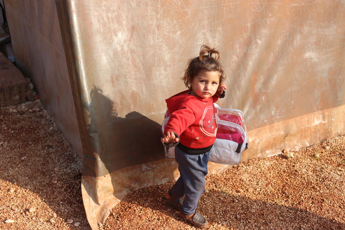 Young child wearing winter clothes and carrying more in Syria