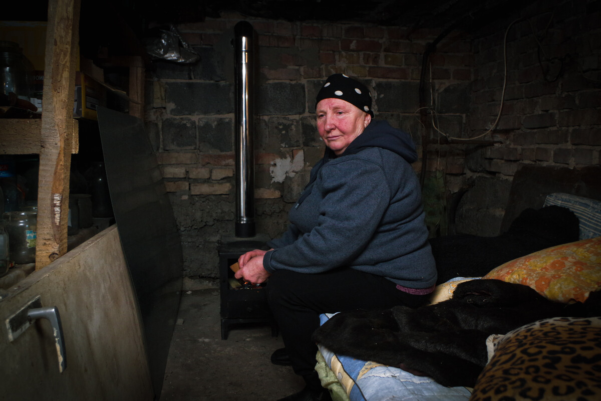 Woman sitting next to a stove in a damaged building in Ukraine.