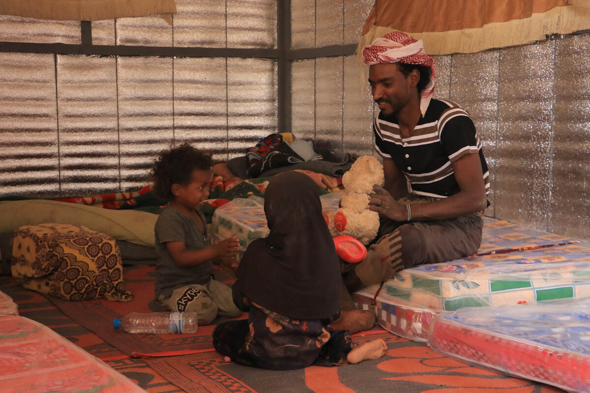 Man and two children sitting inside an iron net shelter in Yemen.