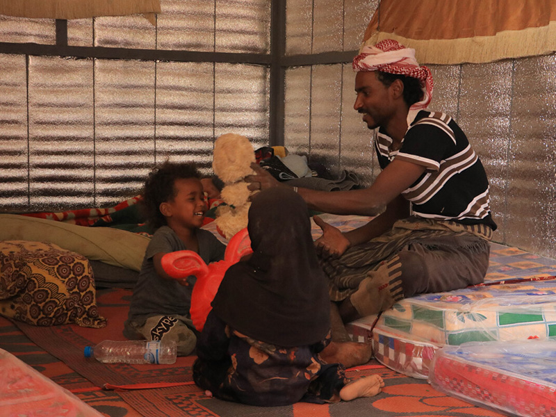 Man playing with two children inside an iron net shelter in Yemen