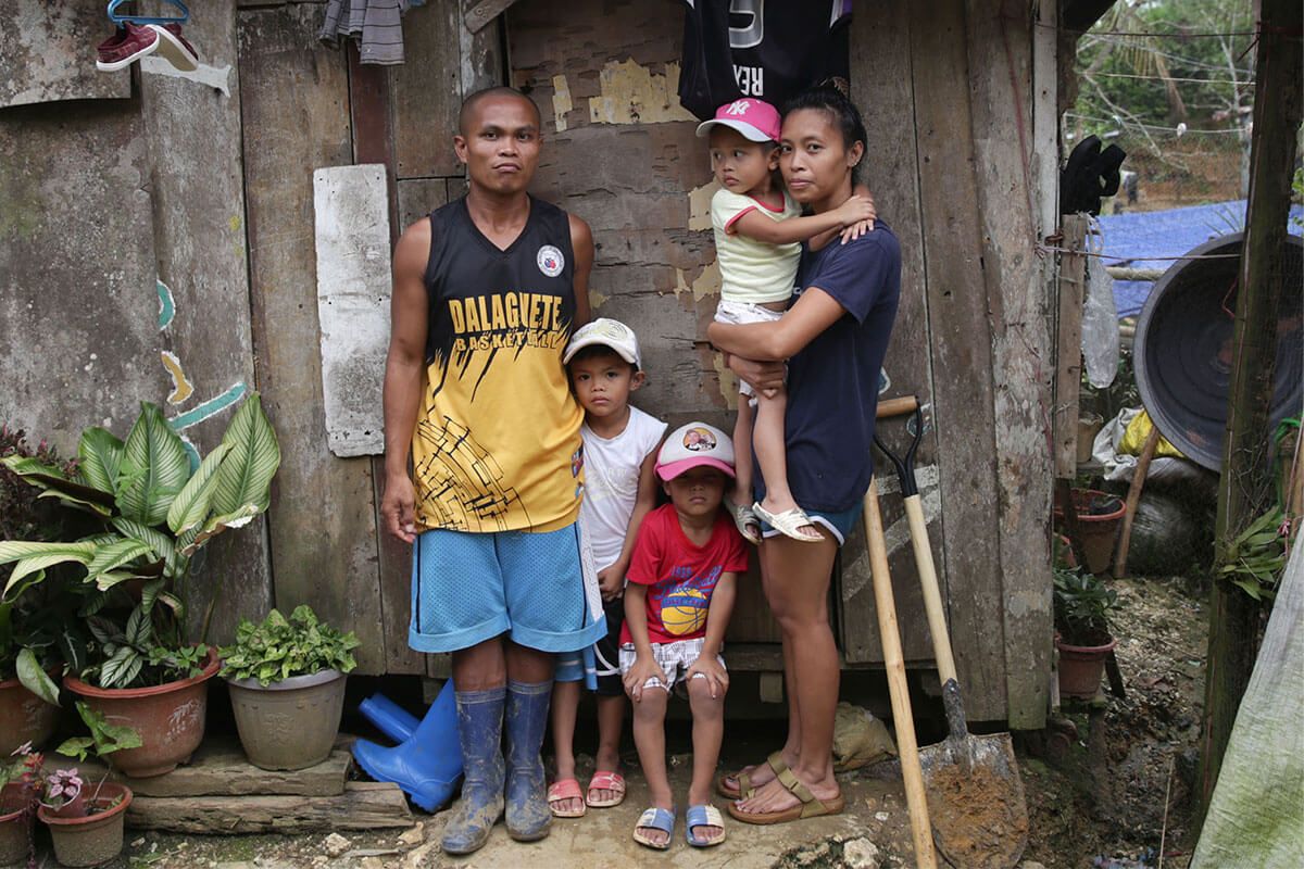 Man, women and three children standing outside a wooden shelter