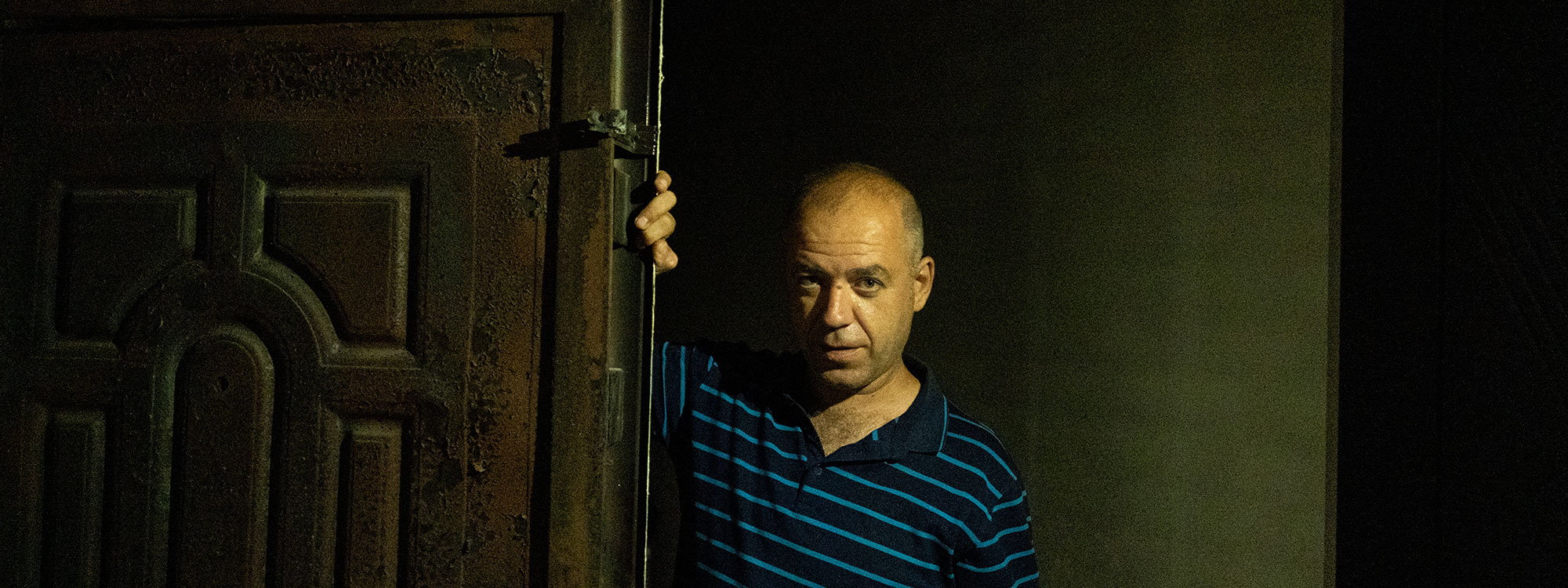 Man stands in darkness leaning on the door of his damaged home in Ukraine