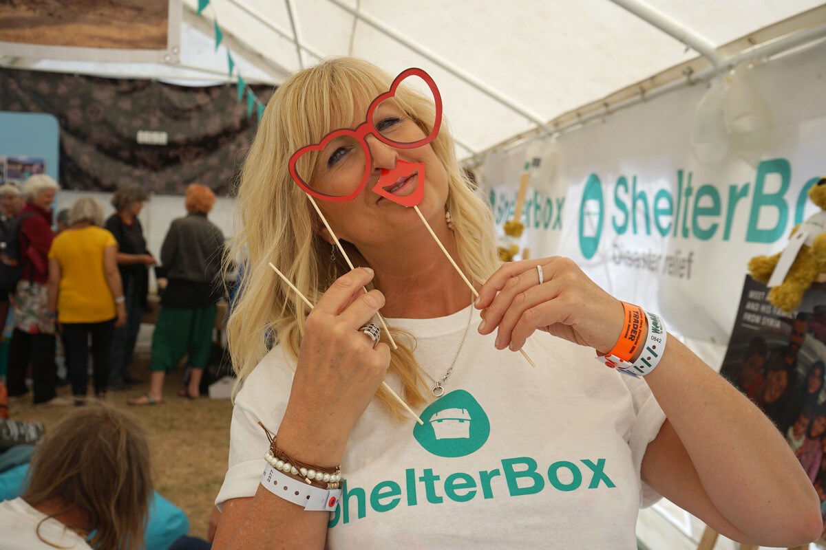 Woman wearing a ShelterBox shirt holding eyeglasses and lip masks in front of her face