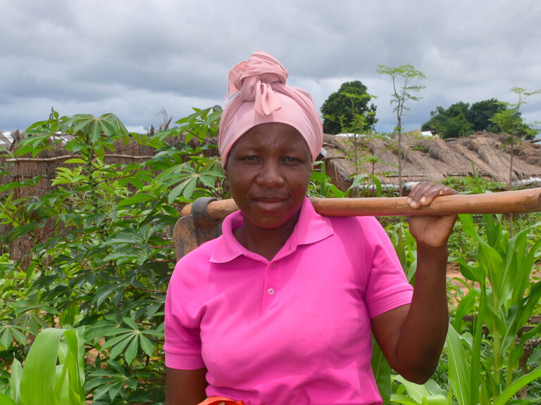 Woman standing among crops holding a hoe in Mozambique