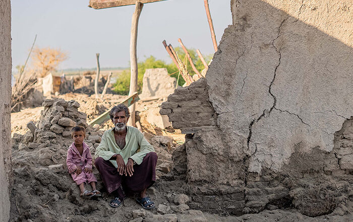 Man and small child sitting in the rubble of a damaged building