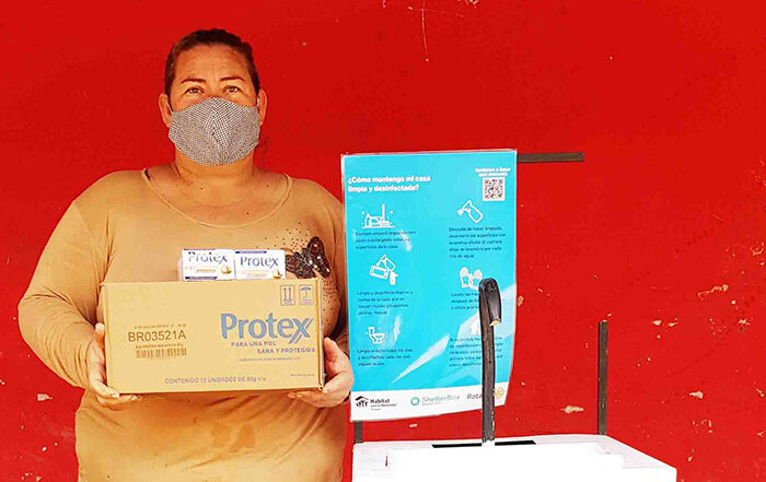 Woman holding box while wearing facemask next to a sign in Paraguay