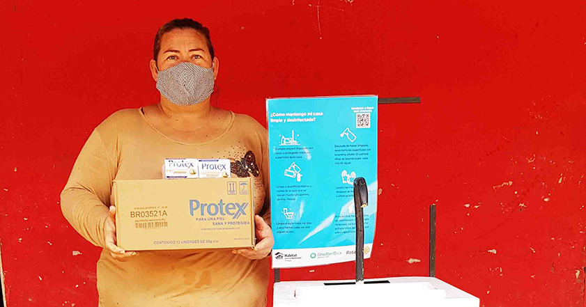 Woman holding box while wearing facemask next to a sign in Paraguay