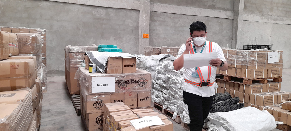 Man wearing a face mask, speaking on the phone and looking at papers at a warehouse at ShelterBox Operations Philippines