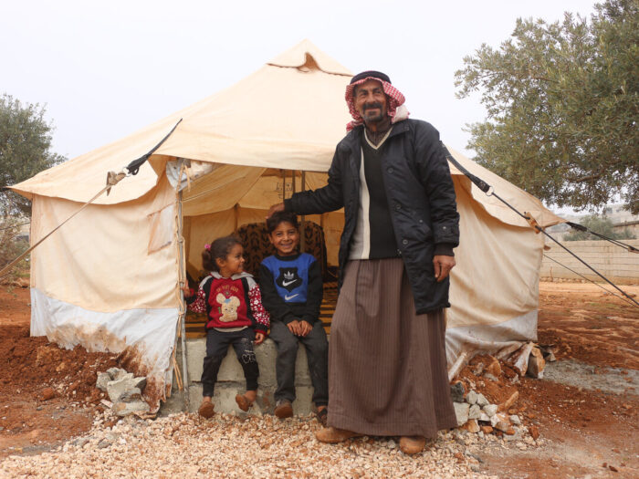Man and two children standing outside a tent in Syria