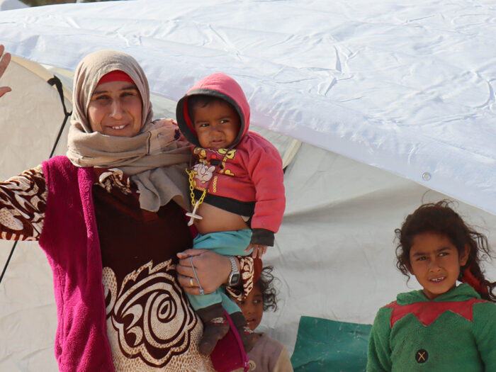 Woman and three children wrapped up in winter clothing outside a tent in Syria