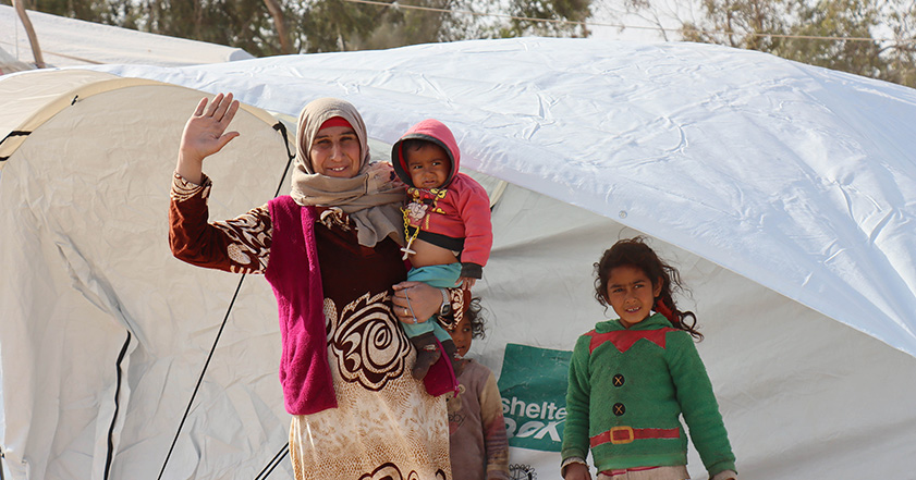 Woman and three children in warm clothes outside a tent in Syria