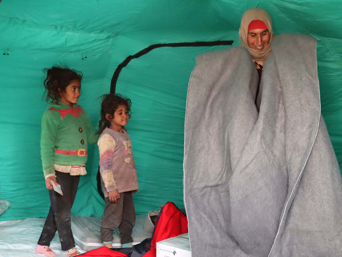 Woman holding a blanket next to her children inside a tent in Syria