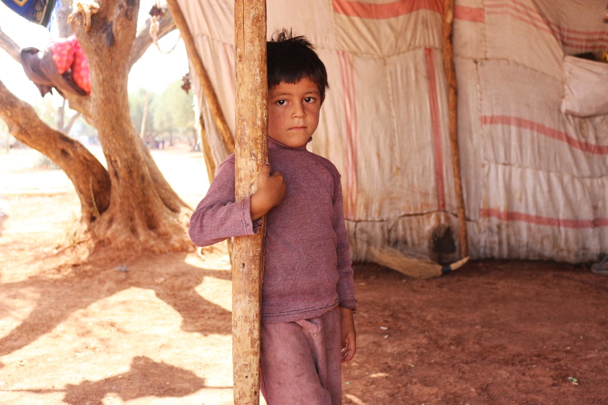 a boy standing next to a pole in a shelter in Syria