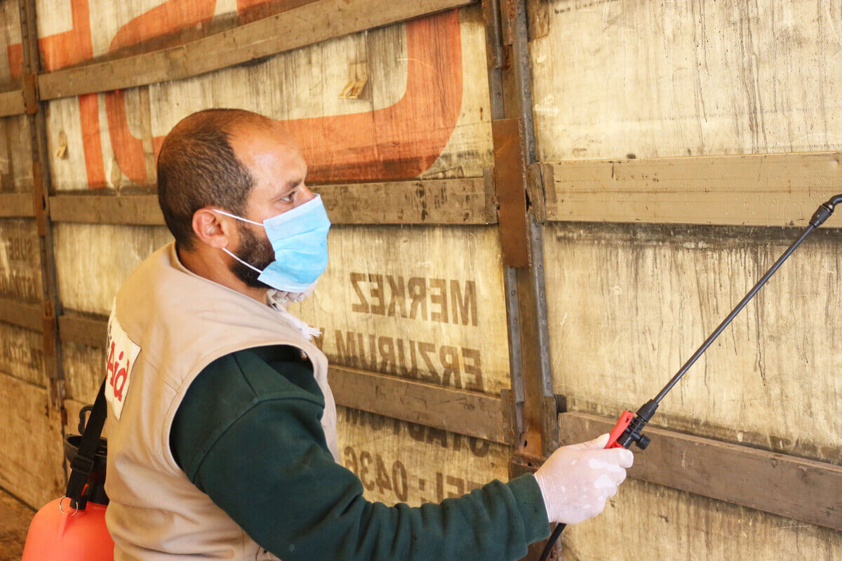 A ReliefAid worker wearing a face mask sprays disinfectant on an aid delivery truck