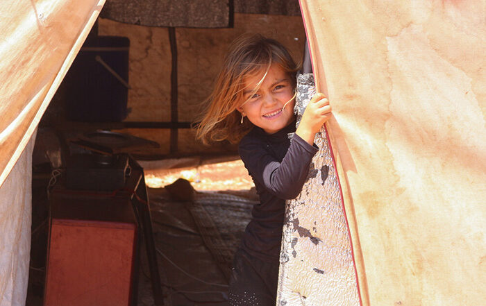 Child smiling while looking through the doorway of a tent in Syria