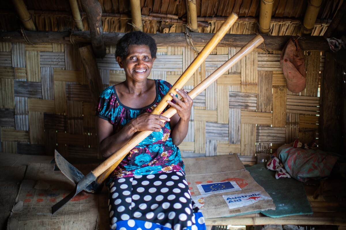 Woman holding farming tools sitting inside a shelter in Vanuatu