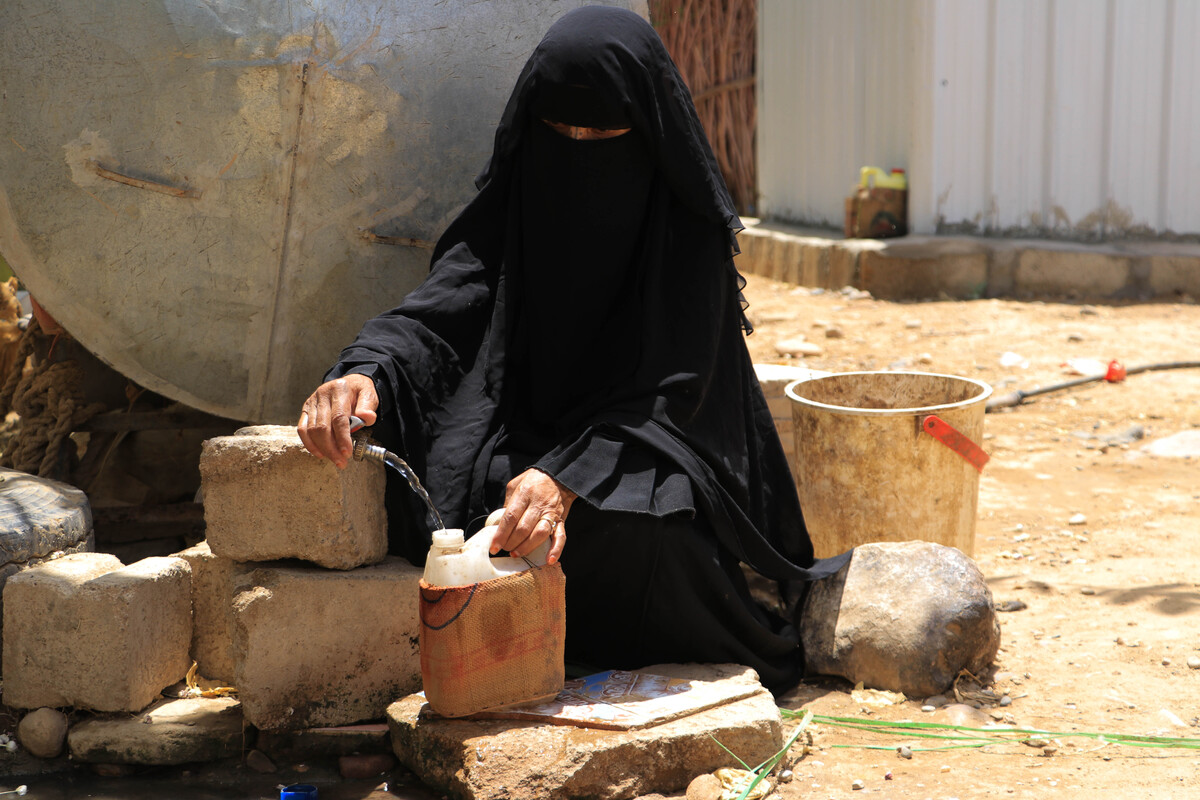 Woman sitting on the floor filling up a water carrier in Yemen
