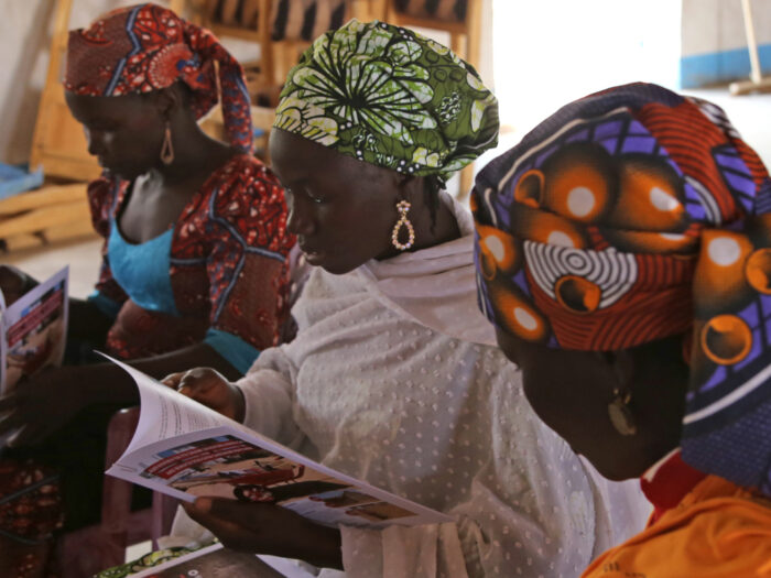Three women looking sitting and looking at paperwork detailing their stories in Cameroon