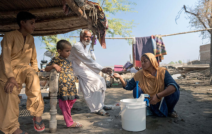 A woman sitting on the ground using a water filter in Pakistan, while family members look on