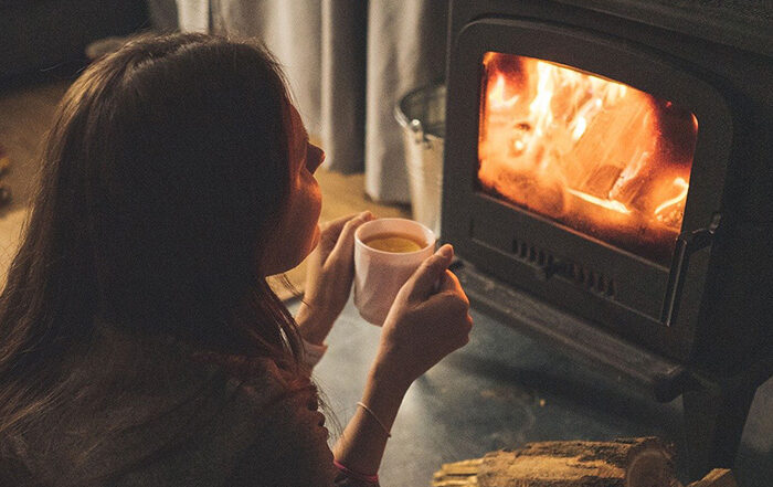 Woman holding cup of tea in front of a fireplace