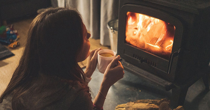 Woman holding cup of tea in front of a fireplace