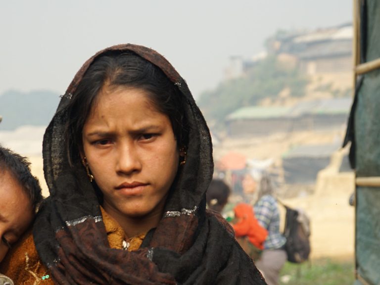 Young woman holding child next to shelters in Bangladesh