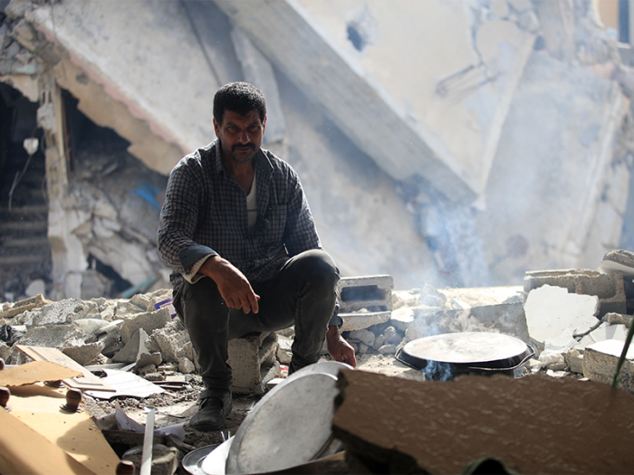 Man crouching in rubble of destroyed buildings Gaza