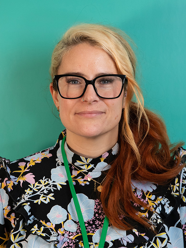 Portrait photo of lady with blond and ginger hair, wearing glasses and a black and white flowery top