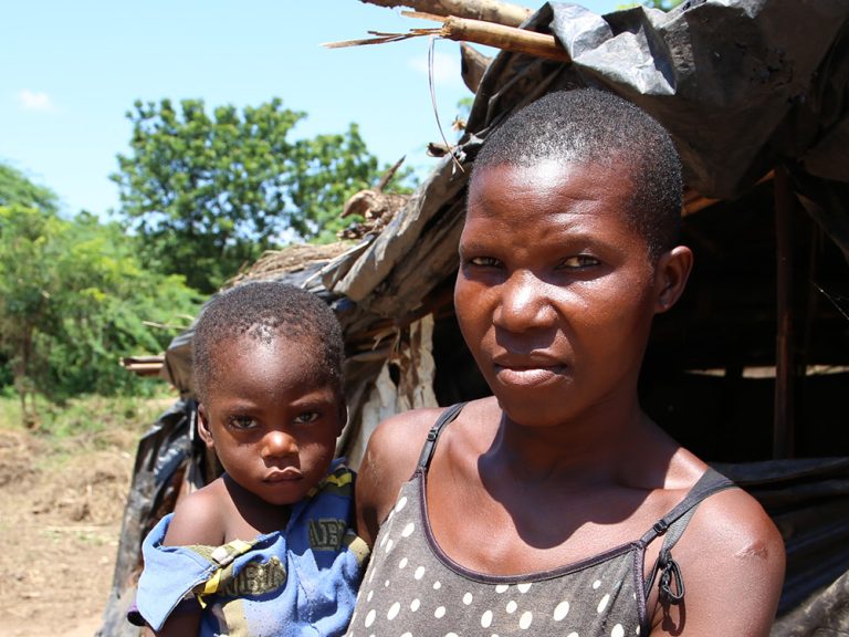 Woman holding a child outside a temporary structure in Malawi