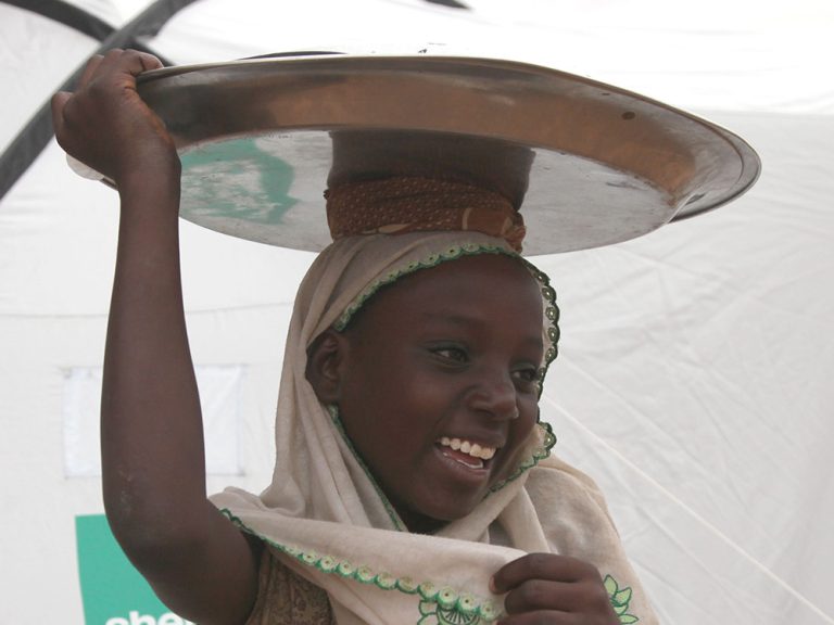 Girl carrying an item on her head outside a tent in Niger