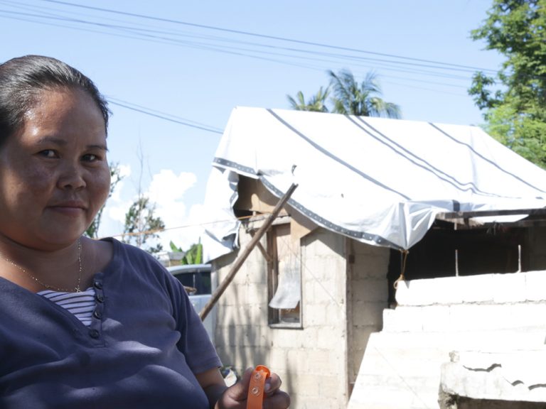 Woman holding solar light standing in front of repaired home in the Philippines.