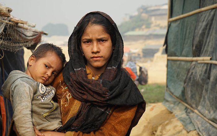 Young woman holding a child next to shelters in Bangladesh