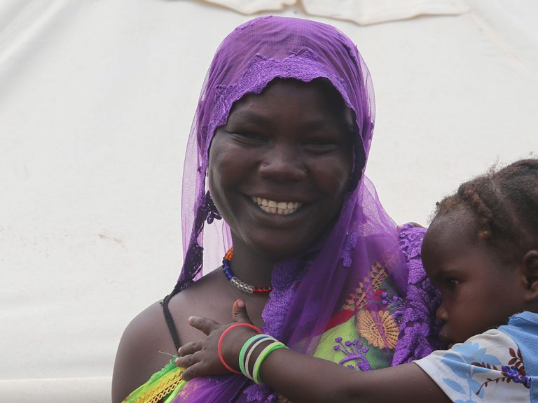 Woman holding a young child in front of a tent in Chad
